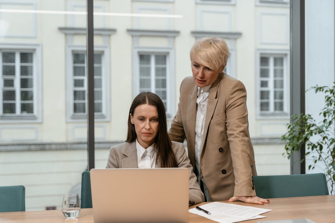 about-02 Two businesswomen in an office setting collaborating with a laptop and documents.
